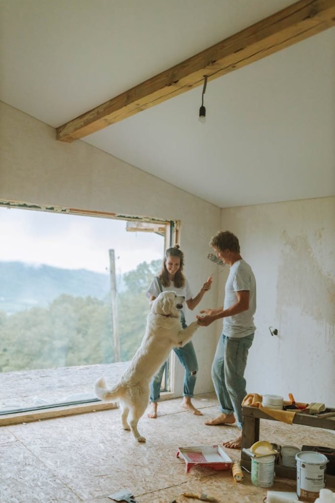 A couple enjoys a playful moment with their dog while renovating their home with large open views.