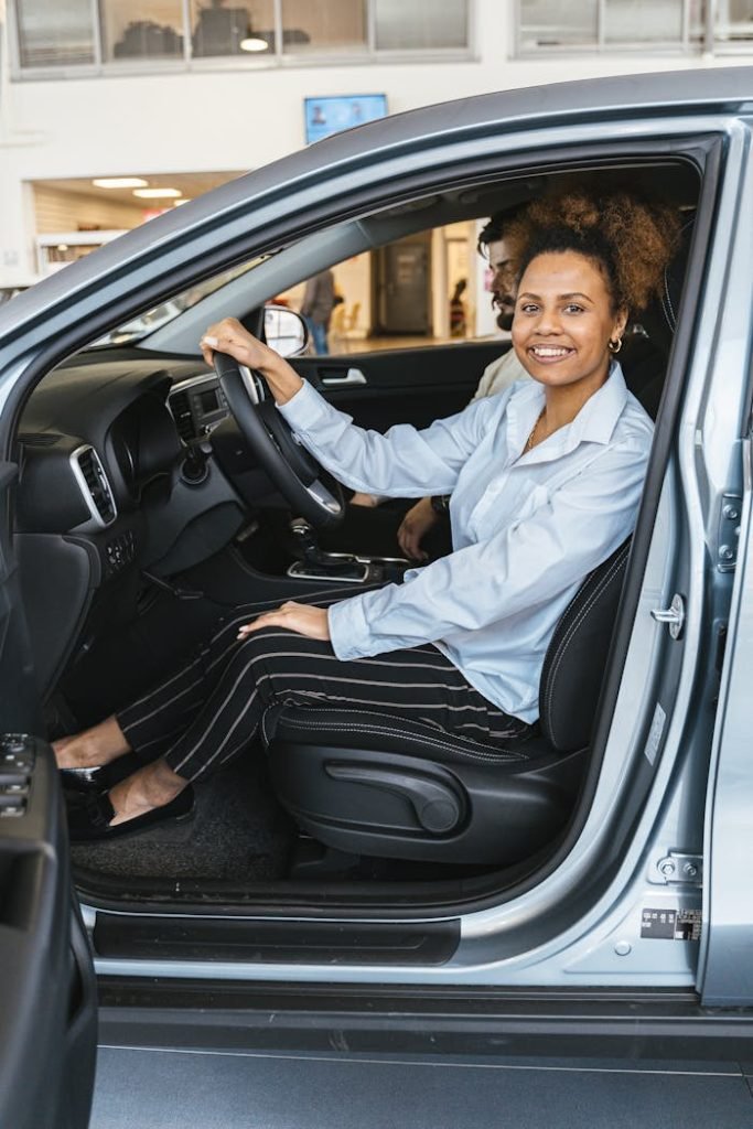 Smiling woman sitting in a car at a dealership, ready for a test drive.